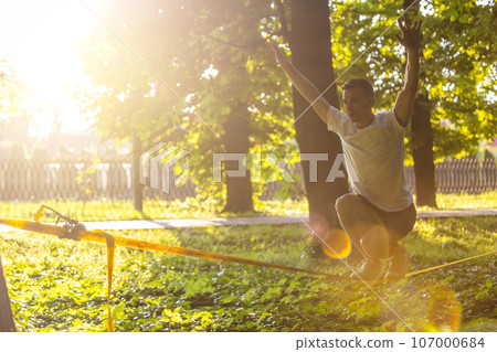Young man balancing on the rope in the forest Young man balancing on the rope in the forest 107000684