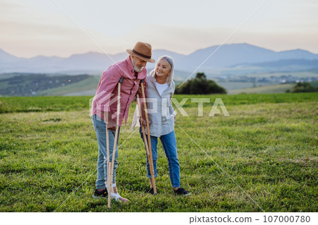 Senior man with broken leg and crutches standing in the the middle of meadow. Senior man with broken leg and crutches standing in the the middle of meadow. 107000780