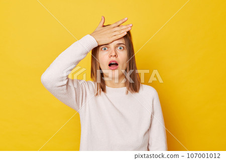 Teenage girl in jumper with ponytails isolated over yellow background makes face palm feeling shocked and scared standing alone looking at camera with big eyes and open mouth. Teenage girl in jumper with ponytails isolated over yellow background makes face palm feeling shocked and scared standing alone looking at camera with big eyes and open mouth. 107001012