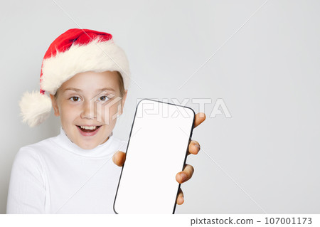 Happy excited Christmas kid Santa showing smartphone with blank empty white screen display Happy excited Christmas kid Santa showing smartphone with blank empty white screen display 107001173