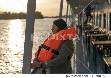 woman wearing an orange life jacket while standing on board a ship 107001868