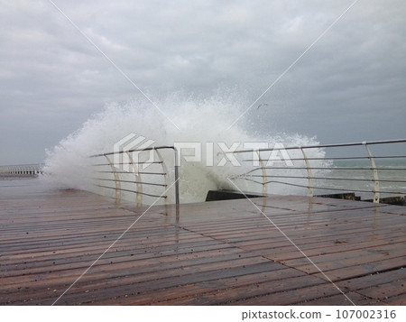 Stormy waves splashing on the wooden decked promenade Stormy waves splashing on the wooden decked promenade 107002316