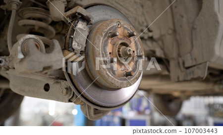 Car brake part in the garage, car brake disc without wheels. Car suspension. Current car repair. Replacement of brake pads in a car service. 107003443