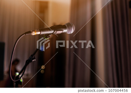 Microphone on stand on stage close up with searchlight light. Professional mic at concert hall or conference room, karaoke, night club, bar. Public events, festival, wedding. Copy space. Microphone on stand on stage close up with searchlight light. Professional mic at concert hall or conference room, karaoke, night club, bar. Public events, festival, wedding. Copy space. 107004456
