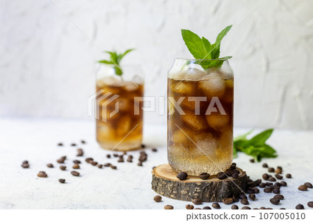 Cold summer cocktail with black coffee tonic mint and ice in glass on white background 107005010