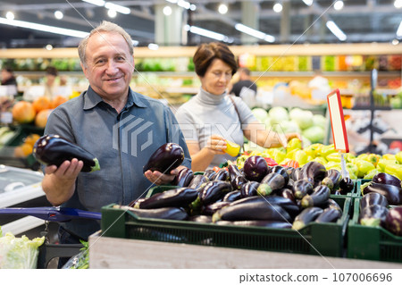 Elderly man chooses eggplants in vegetable and fruit department 107006696