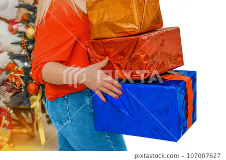 The hands of an adult girl hold a lot of gift colored New Year's boxes in packaging film against the background of a Christmas tree and isolated, white 107007627