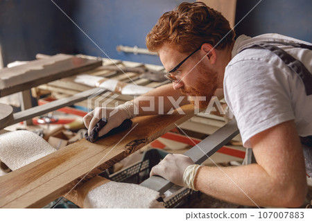Professional carpenter coating a wooden board with protective oil in a workshop. High quality photo Professional carpenter coating a wooden board with protective oil in a workshop. High quality photo 107007883