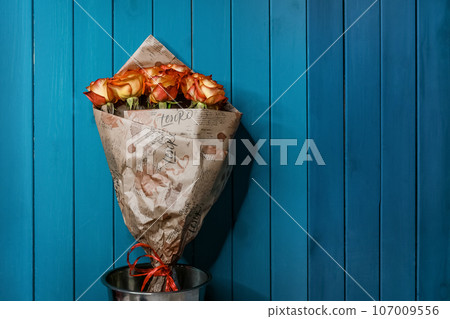 Bouquet of flowers of orange and yellow roses in a decorative paper gift box on a blue wooden background of the interior 107009556