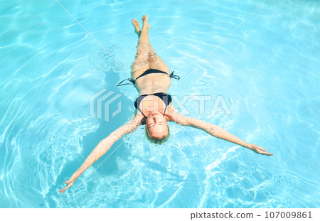 Beautiful Caucasian woman floating in turquoise blue swimming pool. 107009861