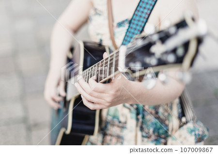 Female street musician playing guitar on sidewalk. 107009867