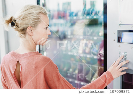 Caucasian woman using a modern vending machine. Her right hand is placed on the dia pad. Caucasian woman using a modern vending machine. Her right hand is placed on the dia pad. 107009871