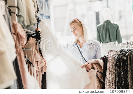 Woman shopping clothes. Female shopper looking at fashionable clothes indoors in clothing store. Woman shopping clothes. Female shopper looking at fashionable clothes indoors in clothing store. 107009874