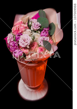 Bouquet of fresh flowers of different colors of roses in paper packaging in a vase on the black background 107009988