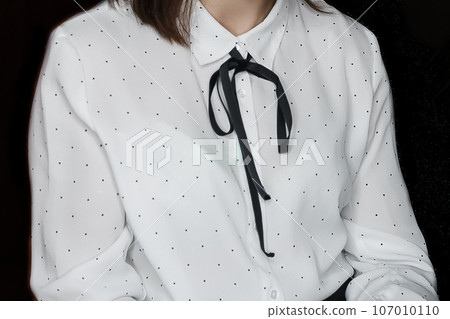 Women's fashion style clothing white blouse with small polka dot pattern with black ribbon tied collar on dark background 107010110