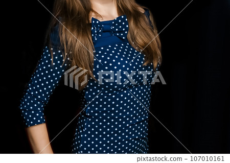 Female skinny figure brunette with long hair in a blue tight-fitting dress with a polka dot pattern on a black background 107010161