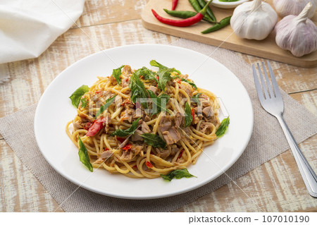 Stir fried Spaghetti with Canned tuna fish and crispy basil leaves in white plate,Spicy pasta Pad Kra Pao.Thai fusion food 107010190