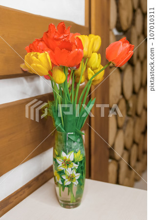 Red and yellow flowers tulips stand in a vase in a wooden interior Red and yellow flowers tulips stand in a vase in a wooden interior 107010311