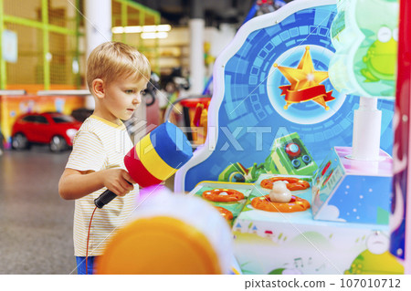 Happy little boy playing fun games on arcade machine at an amusement park 107010712