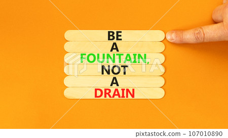 Be fountain not drain symbol. Concept words Be a fountain not a drain on wooden stick. Beautiful orange table orange background. Businessman hand. Business be fountain not drain concept. Copy space. Be fountain not drain symbol. Concept words Be a fountain not a drain on wooden stick. Beautiful orange table orange background. Businessman hand. Business be fountain not drain concept. Copy space. 107010890