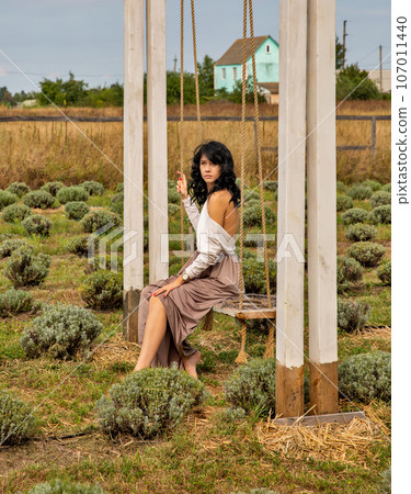 Beautiful young Caucasian woman sitting on a wooden swing. Beautiful young Caucasian woman sitting on a wooden swing. 107011440