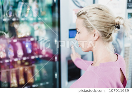 Caucasian woman using a modern vending machine. Her right hand is placed on the dia pad. 107011689