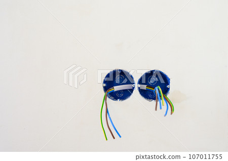Electrical wires sticking out from electrical socket hole on gray concrete wall. 107011755