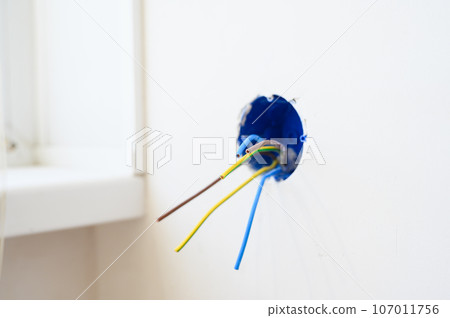 Electrical wires sticking out from electrical socket hole on gray concrete wall. Electrical wires sticking out from electrical socket hole on gray concrete wall. 107011756