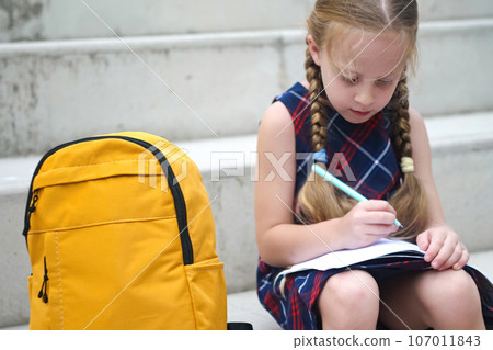 little pupil with a yellow backpack, enthusiastically tackling outdoor homework assignments after school. little pupil with a yellow backpack, enthusiastically tackling outdoor homework assignments after school. 107011843