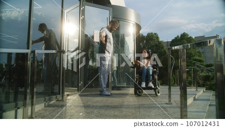 Medical worker opens door to female patient with physical disability 107012431