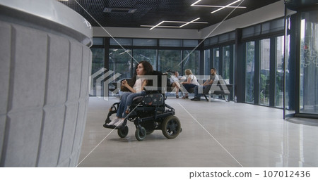 Woman in wheelchair rides to clinic reception and talks with administrator 107012436