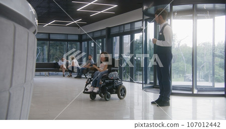 Woman in wheelchair rides to clinic reception and talks with administrator 107012442