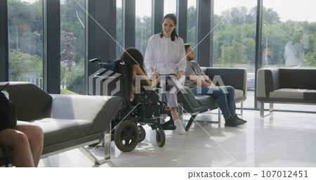 Female physician consults woman in wheelchair in clinic waiting area 107012451