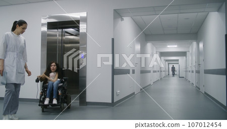 Woman in motorized wheelchair leaves elevator with doctor 107012454