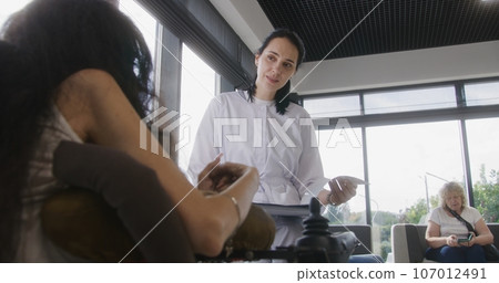 Physician talks to woman with disability in hospital or clinic lobby 107012491