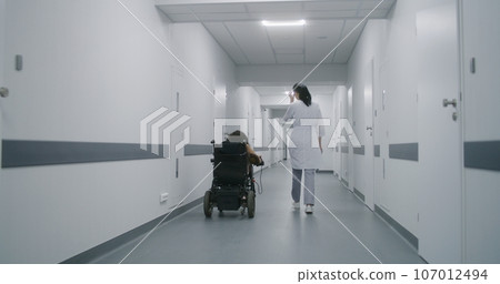 Woman in motorized wheelchair leaves elevator with doctor 107012494