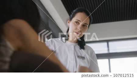 Female doctor consults patient with physical disability in clinic lobby 107012515