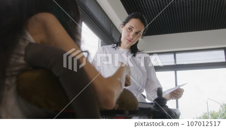 Physician talks to woman with disability in hospital or clinic lobby 107012517