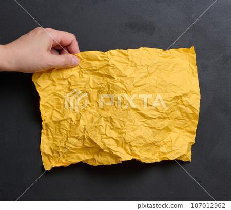 A woman's hand holds a yellow crumpled sheet of paper 107012962