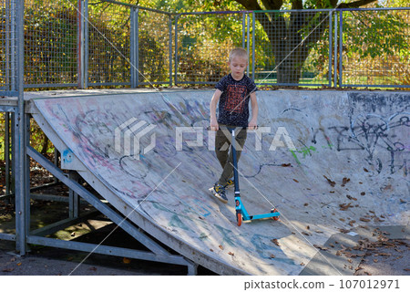 Child on kick scooter in park. Kids learn to skate roller board. Little boy skating on sunny summer day. Outdoor activity for children on safe residential street. Active sport for preschool kid. boy 107012971