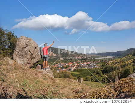 Panorama of Wachau valley (Unesco world heritage site) with man waving hand to valley against Rossatz and Duernstein village in Austria 107012984