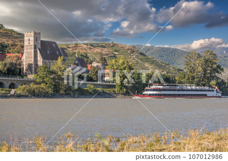 Panorama of Wachau valley (Unesco world heritage site) with ship on Danube river against Sankt Michael church in Lower Austria, Austria 107012986