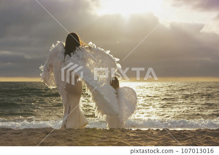 Mom and daughter dressed as angels on the sea at sunset Mom and daughter dressed as angels on the sea at sunset 107013016