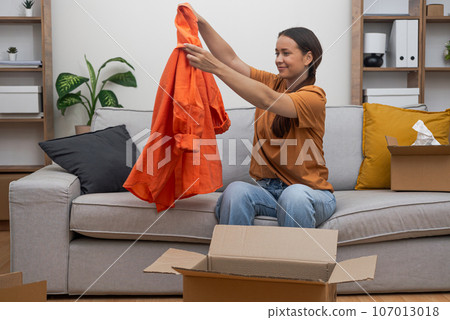 woman unpacks her clothes on her sofa, celebrating her express delivery and e-commerce fashion shopping experience. woman unpacks her clothes on her sofa, celebrating her express delivery and e-commerce fashion shopping experience. 107013018