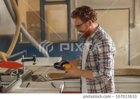 Smiling carpenter in eyeglasses standing on the background on carpentry workshop Smiling carpenter in eyeglasses standing on the background on carpentry workshop 107013610