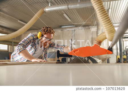 Professional carpenter cutting wooden board at sawmill carpentry manufacturing . Sawing machine 107013620