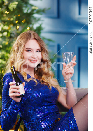 happy attractive woman with bottle and glass of champagne by Christmas tree happy attractive woman with bottle and glass of champagne by Christmas tree 107013634