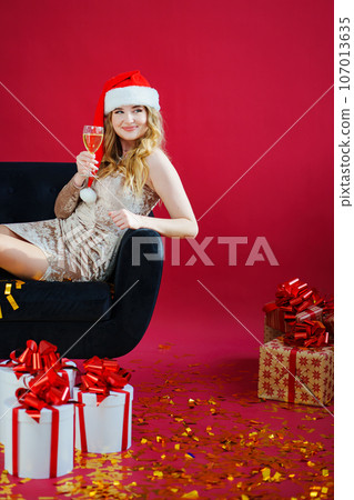 woman in santa hat with champagne and sparklers in red room on sofa with canfeti woman in santa hat with champagne and sparklers in red room on sofa with canfeti 107013635