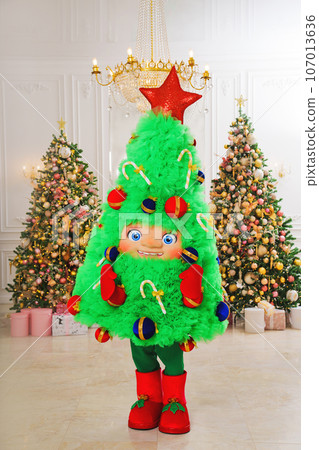 a man in a Christmas tree costume in a room with christmas decor and firs a man in a Christmas tree costume in a room with christmas decor and firs 107013636