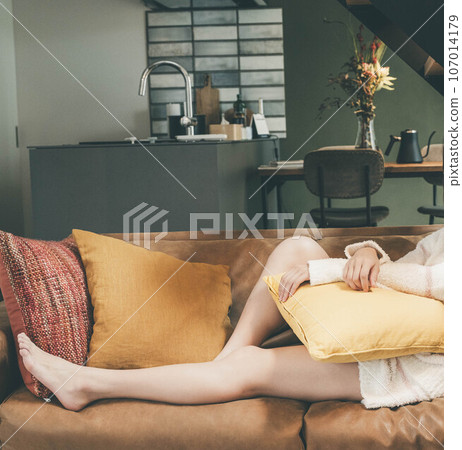 A woman relaxing on the sofa in the living room with her legs stretched out 107014179